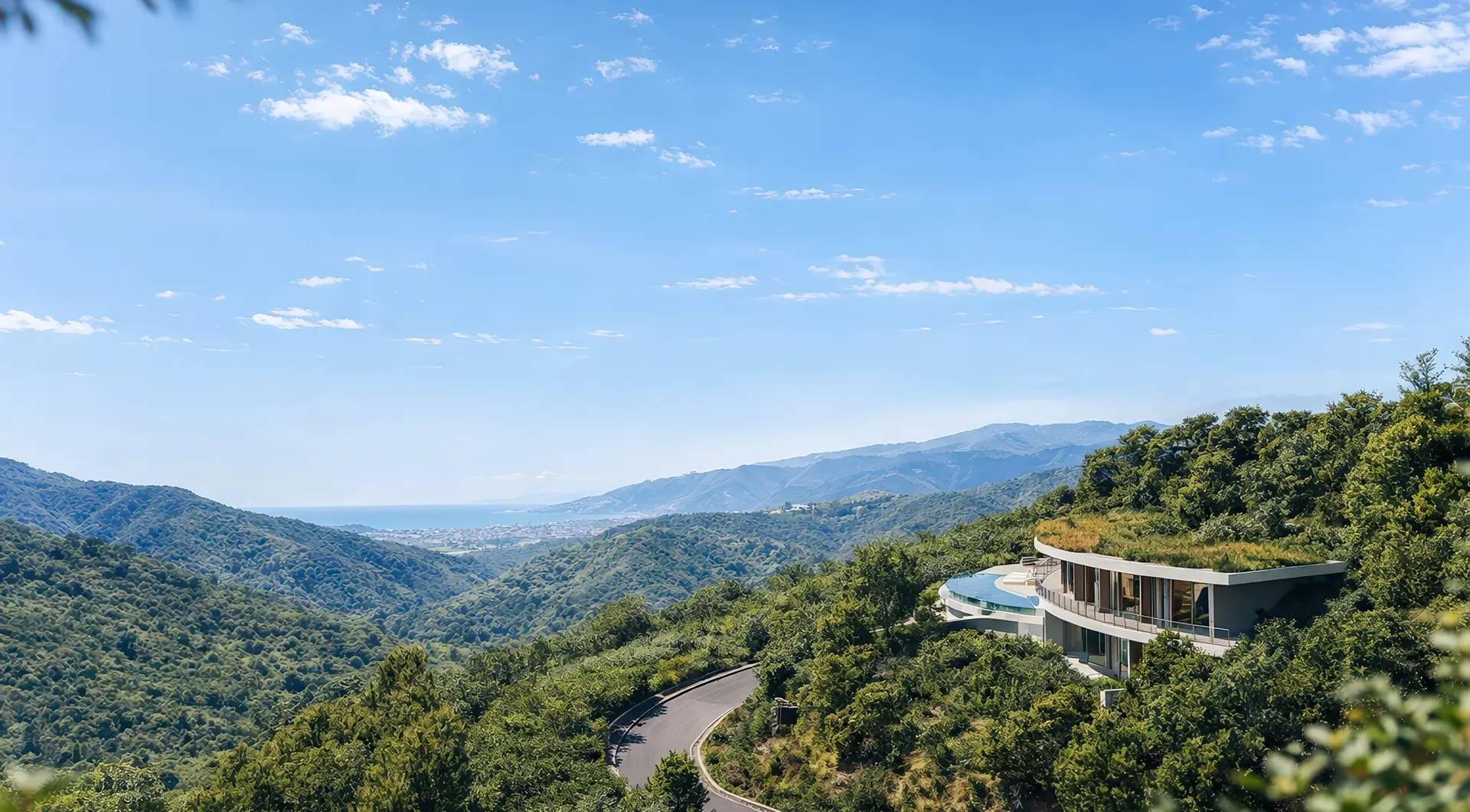 Contemporary curved villa with a green roof and expansive glass walls, nestled on a lush mountainside. The home overlooks rolling green hills, a winding road, and distant ocean views under a clear blue sky, creating a secluded luxury retreat in nature.