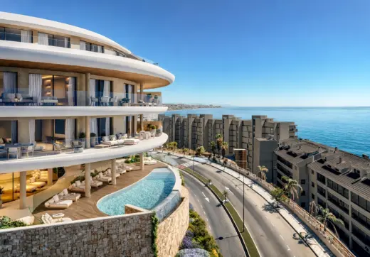 Luxury beachfront development in Fuengirola Carvajal featuring curved contemporary architecture with spacious glass-fronted terraces, an infinity pool overlooking the Mediterranean Sea, and panoramic coastal views along the shoreline.