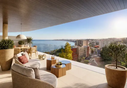 Luxury terrace in Fuengirola Carvajal featuring comfortable outdoor lounge seating, wooden coffee tables, large potted plants, glass balustrades, and breathtaking panoramic views of the Mediterranean coastline and city skyline at sunset.