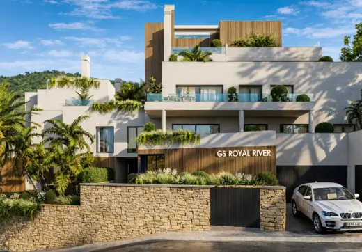 Entrance of Royal River Marbella modern residential building with terraces, greenery, stone wall and parked car.